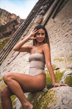 A dark-haired caucasian woman in a brown swimsuit on a natural background next to rocks and sea in the town of Zumaia