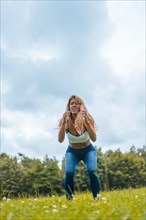 Fitness session with a young blonde caucasian woman exercising in nature with a blue maya on her feet and a white short shirt. Squatting and jumping