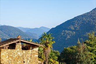 Beautiful Panoramic View over Mountain Range and Valley and Rustic Hut and Palm Tree with Sunlight and Clear Blue Sky in Malcantone