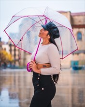 Street Style of a young brunette Latina in the rain of the city with an umbrella