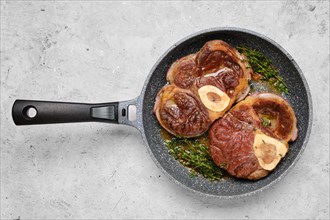 Two pieces of beef meat ossobuco in a frying pan with thyme