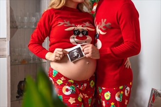 Young couple with red Christmas decorations and clothes having an ultrasound of the new child for the family. Family with pregnant woman