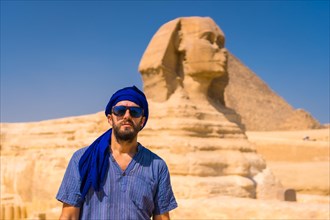 Portrait of a young tourist dressed in blue and a blue turban at the Great Sphinx of Giza. Cairo