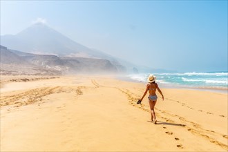 A young woman walking alone on the wild Cofete beach of the Jandia natural park
