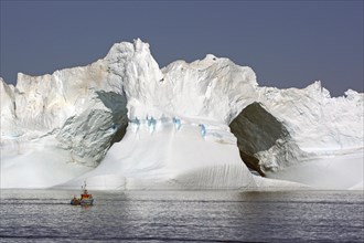 Small fishing boat in front of huge iceberg with large ice gates
