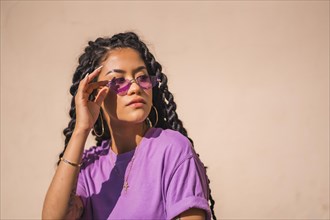 A young dark-skinned woman with purple glasses in an urban session of Latin ethnicity