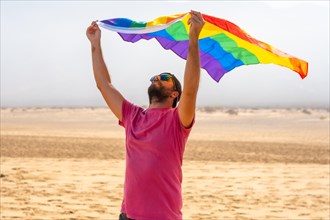A gay person with the LGBT flag enjoying it moving with the wind in a desert