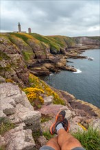 A young tourist sitting on the coast next to the Phare Du Cap Frehel