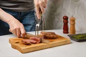 Hand of man cutting beef steak with knife on kitchen table