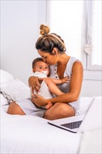 Young Caucasian mother with her son in the room on top of the bed. Baby less than a year learning the first lessons of her mother. Hugging him and giving him love