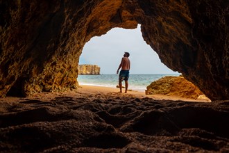 A man in the natural cave in the Algarve in summer on the beach at Praia da Coelha