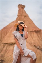 Sensual gazes of a brunette Caucasian girl in an explorer outfit with a white dress and a hat in a desert on a cloudy afternoon