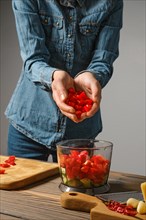Unrecognizable woman pours finely chopped bell pepper into blender bowl