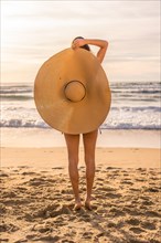 Vertical photo of a woman with big sun hat on the beach