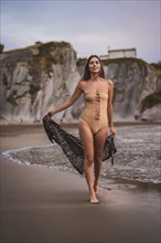 A brunette woman with a swimsuit and a pareo walking on the beach in summer