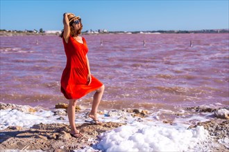 Girl with red dress and straw hat in the pink lagoon of Torrevieja