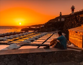 A young man sitting in the sunset of the Fuencaliente Lighthouse next to the salt mine