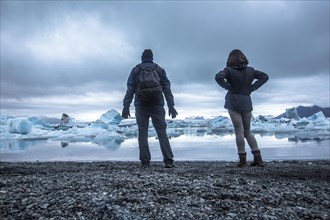A couple with a backpack looking at the Jokulsarlon Ice Lake in the golden circle of southern Iceland