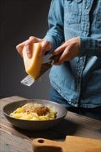 Unrecognizable woman grates parmesan cheese into pasta