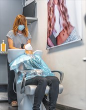 Hairdresser with face mask washing hair to client. Safety measures for hairdressers in the Covid-19 pandemic. New normal