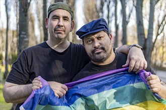 Gay couple in a park holding lgbt rainbow flag