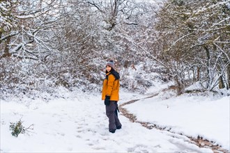 A young woman in a yellow jacket walking along the path of frozen trees. Snow in the town of Opakua near Vitoria in Araba