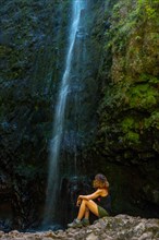 Unrecognizable young woman sitting in the waterfall at the Levada do Caldeirao Verde