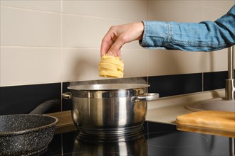 Unrecognizable woman drops fettuccine pasta into saucepan with boiling water
