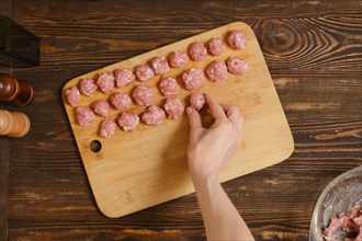Top view of female hand putting meatball on a board in a row