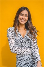 A pretty brunette smiling with a yellow background behind