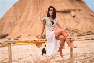 Sensual looks from a brunette Caucasian girl in an explorer outfit with a white dress sitting in the desert