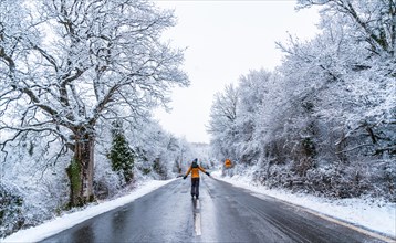 A young woman in a yellow jacket walking along an icy road and denied trees. Snow in the town of Opakua near Vitoria in Araba