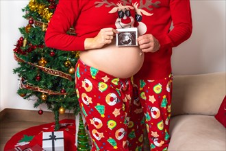 Young couple with red Christmas decorations and clothes having an ultrasound of the new child for the family. Family with pregnant woman