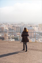 A young tourist girl at sunrise at the viewpoint of Cerro San Cristobal and the city of Almeria in the background