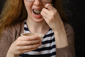 Unrecognizable young woman in glasses eating yogurt