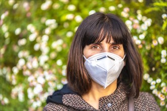 Portrait of a young woman with a mask next to a beautiful daisies. First walks of the uncontrolled Covid-19 pandemic