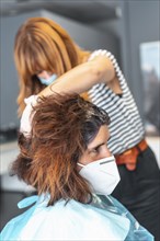 Hairdresser with face mask giving the dye to the client. Safety measures for hairdressers in the Covid-19 pandemic. New normal