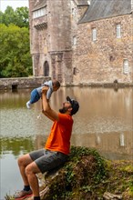 A young father with his baby visiting the medieval lakeside Chateau Trecesson