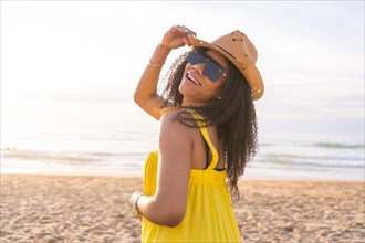 Sensual woman wearing sunglasses and sun hat posing smiling to the camera on the beach