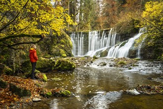 The Geratser waterfall in autumn. A hiker stands on the bank. Moss-covered rocks on the sides