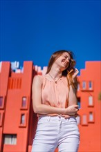 Lifestyle of a young Caucasian woman in a salmon colored shirt and white pants smiling in some beautiful colored houses