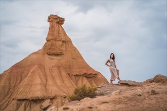 Brunette Caucasian girl in a white dress and a straw hat in a beautiful desert on a cloudy afternoon