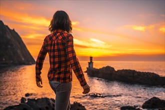 A young woman in a plaid shirt watching the sunset from the Pasajes San Juan lighthouse