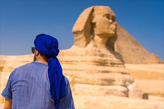 A young tourist enjoying and admiring the Great Sphinx of Giza dressed in blue and a blue turban. Cairo
