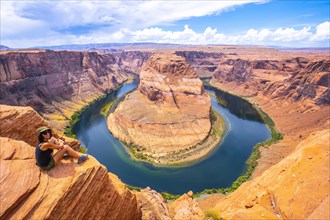 A tourist sitting on Horseshoe Bend and the Colorado River in the background