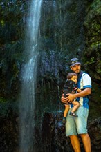 A father with his son in his backpack at the waterfall at Levada do Caldeirao Verde