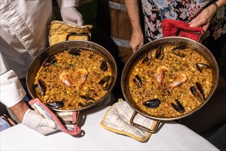 Two cooks with seafood paellas