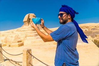 A young man putting on the mask facing the Great Sphinx of Giza and the Pyramids of Giza in the background