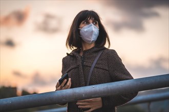 A young brunette with a mask on a sunset on a bridge. First walks of the uncontrolled Covid-19 pandemic