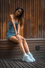 Portrait of a pretty brunette girl sitting on a wooden chair in a denim skirt